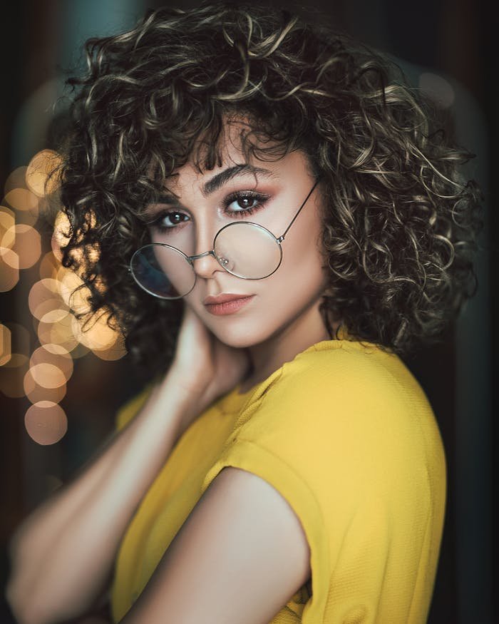 About Stylish portrait of a woman with curly hair and eyeglasses in a vibrant setting.